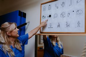 Physiotherapeutin zeigt auf eine Tafel mit Piktogrammen, mit denen Sie mit zugewanderten Kindern kommunizieren kann