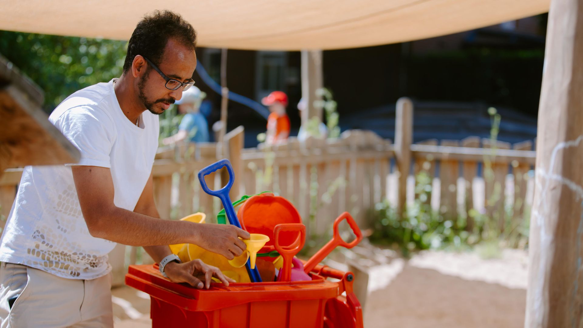 Kita-Mitarbeiter räumt Sandspielzeug zusammen