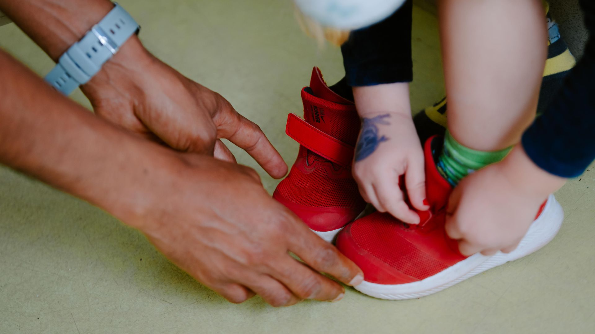 Kita-Mitarbeiter hilft Kind beim Schuhe anziehen