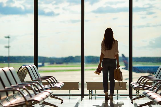 Frau steht mit Pass und Reisegepäck am Flughafen